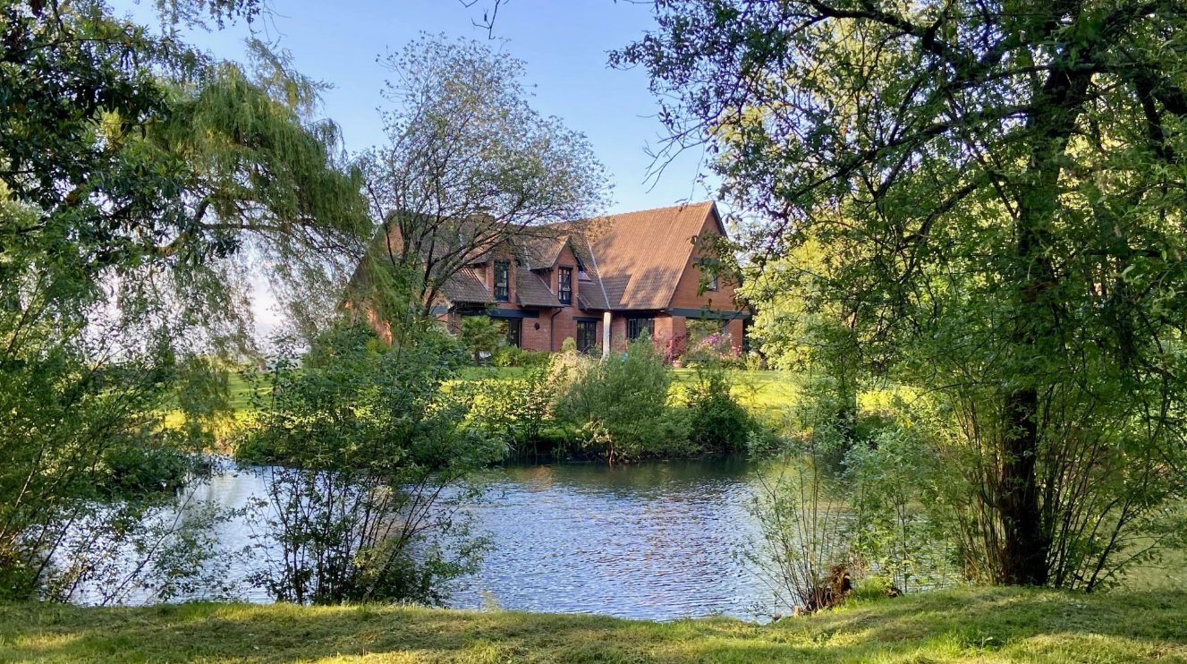 La maison de La Tribu de Saint-Josse, en briques, derrière l'étang et les arbres